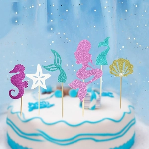 Close-up of glittery mermaid tail and seashell cake toppers on a blue ocean-themed cake