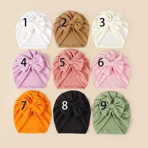 Macro display of nine colorful knitted baby turbans with large bows and ribbed texture