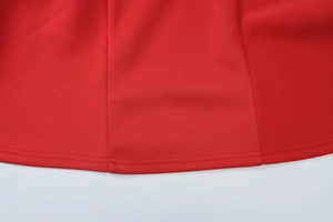 Detailed macro view showing the double-stitched hem and fabric texture of a red dress