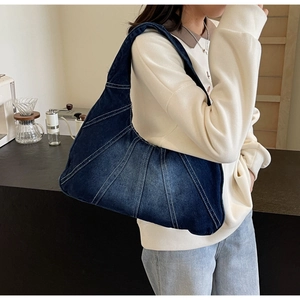 Détail du sac à épaule en jean bleu foncé avec surpiqûres, porté par un mannequin en café