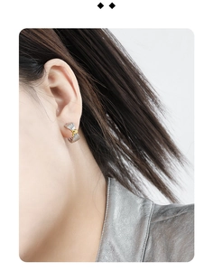 Detailed view of silver knot stud earring with gold accent on ear for size reference