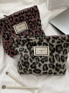 Fuzzy leopard print makeup bags in pink and gray on a minimalist linen background