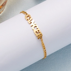 Gold stainless steel Cancer zodiac letter bracelet with Cuban chain links on white stand