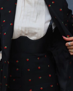 Vue détaillée des broderies fraises rouges sur le blazer noir et l'ensemble jupe
