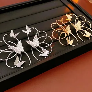 Golden and silver wire-wrapped floral butterfly earrings on a black jewelry stand