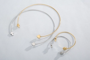 Detail of gold and silver open bracelets featuring heart and cross charms on textured grey surface