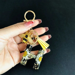 Close-up of resin letter H keychain with real yellow daisies, gold bee and tassel charm