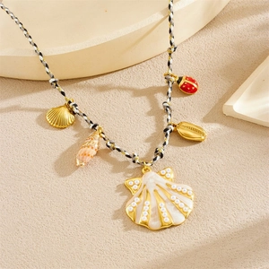 Detail of woven rope necklace with shell pendants and gold ladybug on sand texture