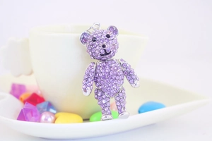 Close-up of a teddy bear keychain fully encrusted with purple rhinestones on a ceramic cup