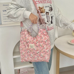 Detail of pink floral quilted handbag featuring a woven handle and adjustable strap