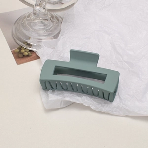 Close-up of matte grey-green rectangular hair claw clip on white textured paper