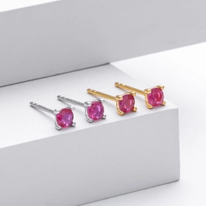 Detailed view of four-prong red gemstone stud earrings in silver and gold finishes