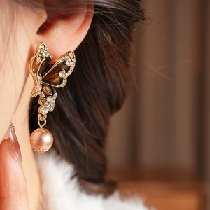 Close-up of vintage butterfly earring with enamel, rhinestones and a pearl drop pendant