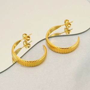 Detail of golden textured hoop earrings featuring horizontal grooves on a mirror surface