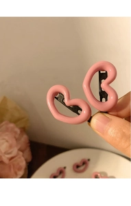 Close-up of two sweet pink heart-shaped metal hair clips held by hand in soft light