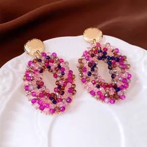 Chic multi-color beaded oval earrings with golden metallic studs on white ceramic plate