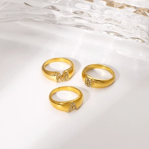 Minimalist gold letter rings M, B, A with sparkling rhinestones on white surface
