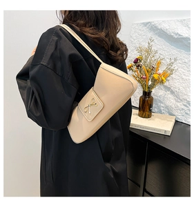 Detail of beige shoulder bag with a small gold bow clasp held by a model in a room