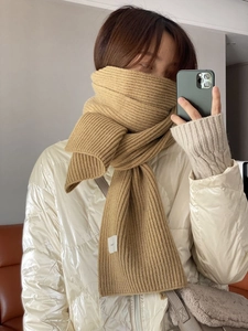 Detail of camel chunky knit scarf showing thick ribbed texture and brand label on person