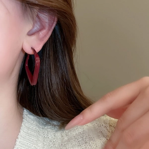 Close-up of deep red geometric triangular hoop earrings with polished glossy finish