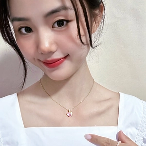 Gros plan d'un collier pendentif cœur rose sur chaîne dorée porté par une femme modèle