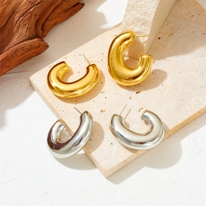 Polished gold and silver hollow G-shaped earrings on natural stone and wood