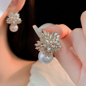 Detailed close-up of matte gold flower earrings with crystals and a large white pearl