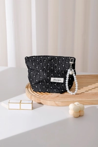 Detail of black polka dot pouch with ruched texture, white spots, and elegant pearl charm
