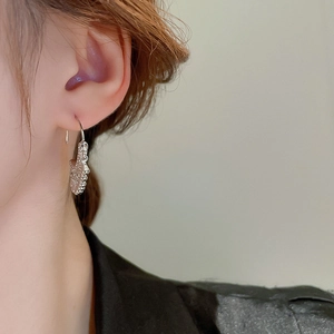 Close-up of a silver textured metal earring with irregular water drop design on a model