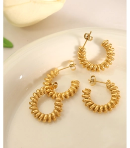 Detail of four gold twisted C-shape earrings displayed on white ceramic with tulips