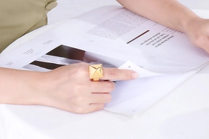 Close-up of golden pyramid stud ring worn by model while reading a magazine