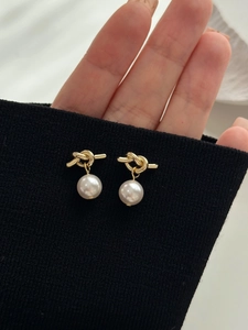 Close-up of golden knot earrings with round white pearl drop on black knit background