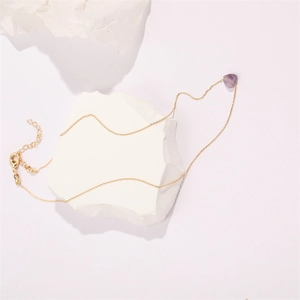Detail of a gold-plated heart-shaped amethyst pendant with lobster clasp on a white stone