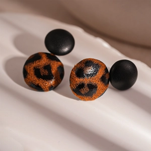 Macro view of leopard print and black leather heart-shaped geometric stud earrings