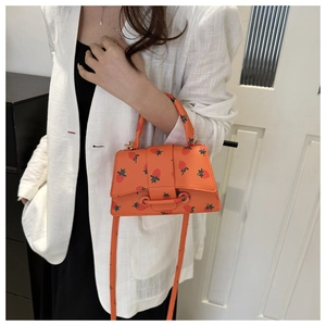 Detailopname van een mini oranje trapeziumtas met aardbeienprint en schouderband