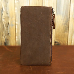 Macro detail of brown leather wallet showing stitching and metal zipper on wood background