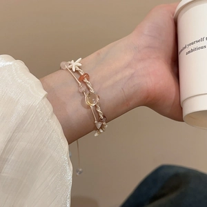 Detail eines geflochtenen Armbands mit Natursteinen und Seestern-Anhänger am Handgelenk