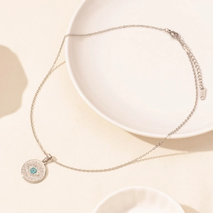 Detail of silver stainless steel chain with blue stone Evil Eye pendant on white ceramic
