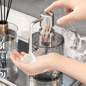 Elegant gray glass soap dispenser with chrome pump on marble surface being pressed