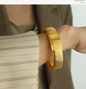 Detail of a flexible gold-plated ribbed bracelet on wrist with a matte rectangle clasp