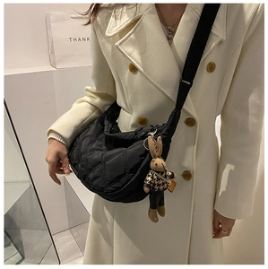 Detail of black quilted crescent crossbody bag with cute bunny doll on a model