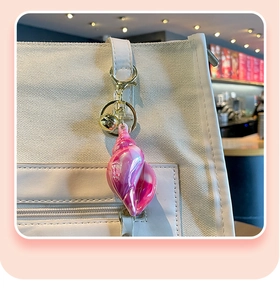 Pink gradient conch keychain with golden bell hanging on white canvas bag
