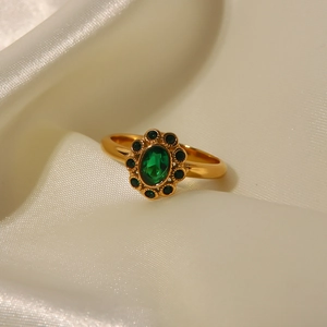 Macro shot of gold floral ring with oval emerald gemstone on soft beige silk fabric