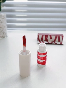 Detail of red matte lip mud brush and white tube with wave patterns on a white table