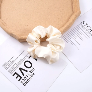 Detailed texture of cream satin oversized scrunchie on a cork tray with aesthetic cards