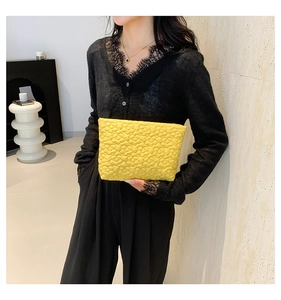Detail of yellow quilted bubble clutch bag held by a model in black lace clothing