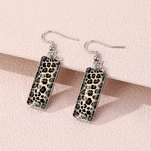 Macro detail of rectangular leopard print earrings with silver metal hooks on pink surface