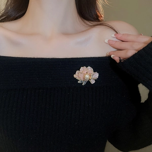 Detail of a 3D pink floral brooch with pearl center pinned on a black knit garment