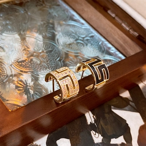 Detail of gold C-shaped earrings with rhinestones and black enamel on a wooden frame