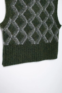 Gros plan du gilet en maille à losanges montrant la texture laine et l'ourlet côtelé